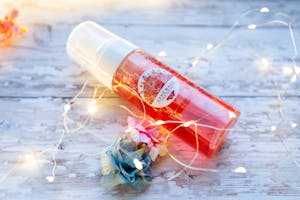 Charming floral essence bottle surrounded by delicate fairy lights on a rustic wooden table.