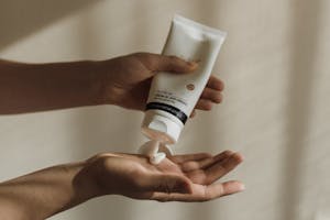 Close-up of a woman squeezing lotion onto her hand, emphasizing skincare and self-care routine.