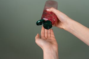 Close-up of hands dispensing liquid gel from a bottle with green cap.