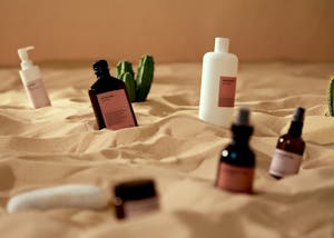 Cosmetic and skincare products artistically arranged on sand with cactus accents, evoking a desert vibe.