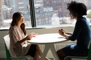 Two professional women having a discussion at a desk in a bright office setting.