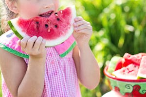 Young girl eating a juicy watermelon slice in a sunny outdoor setting, symbolizing summer refreshment.